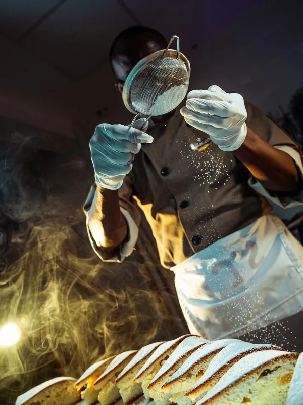 Pâtissier tamisant de la farine au-dessus d’une fournée