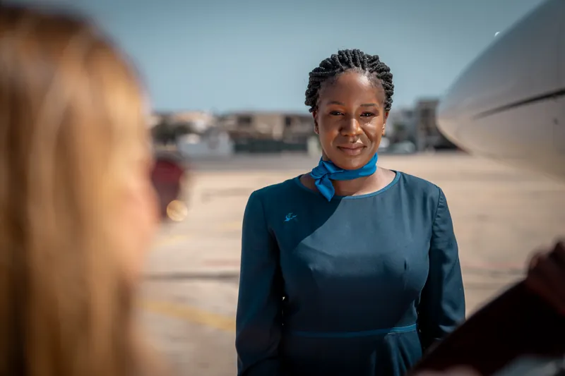 Hôtesse SamAirways accueillant une passagère au pied de l’avion